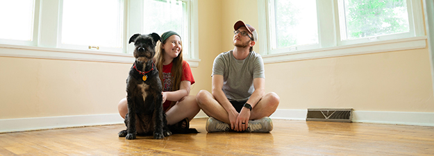 man, woman and dog sit on floor of empty room imagining their future home