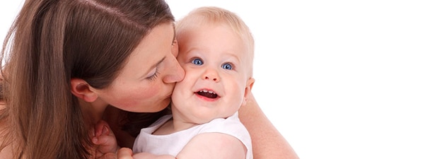 A woman with long brown hair kisses a smiling baby on the cheek. The baby, with bright blue eyes and light hair, looks content and is wearing a white sleeveless outfit. The embrace speaks volumes about love and custodial rights. The background is white.