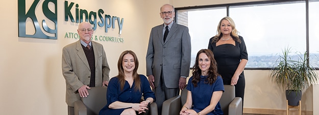 A group photo of five professionals, three men and two women, posing in an office near a window. Two women are seated in the front while the three men stand behind them. The office wall features the "KingSpry Attorneys & Counselors" logo on the left side, reflecting their expertise in Family Law.